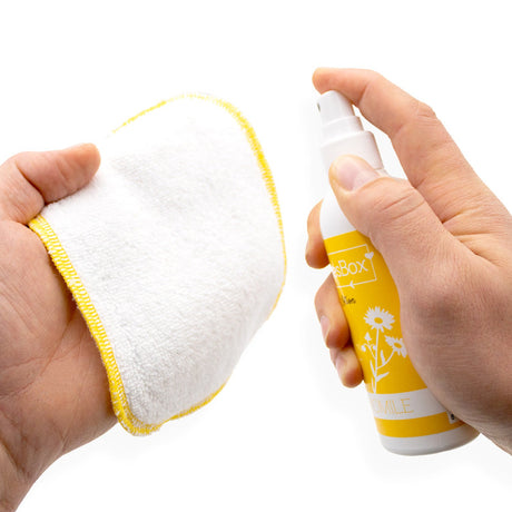 Hand sprüht Billies Box Lotion Kamille auf einen waschbaren Waschlappen mit gelbem Rand