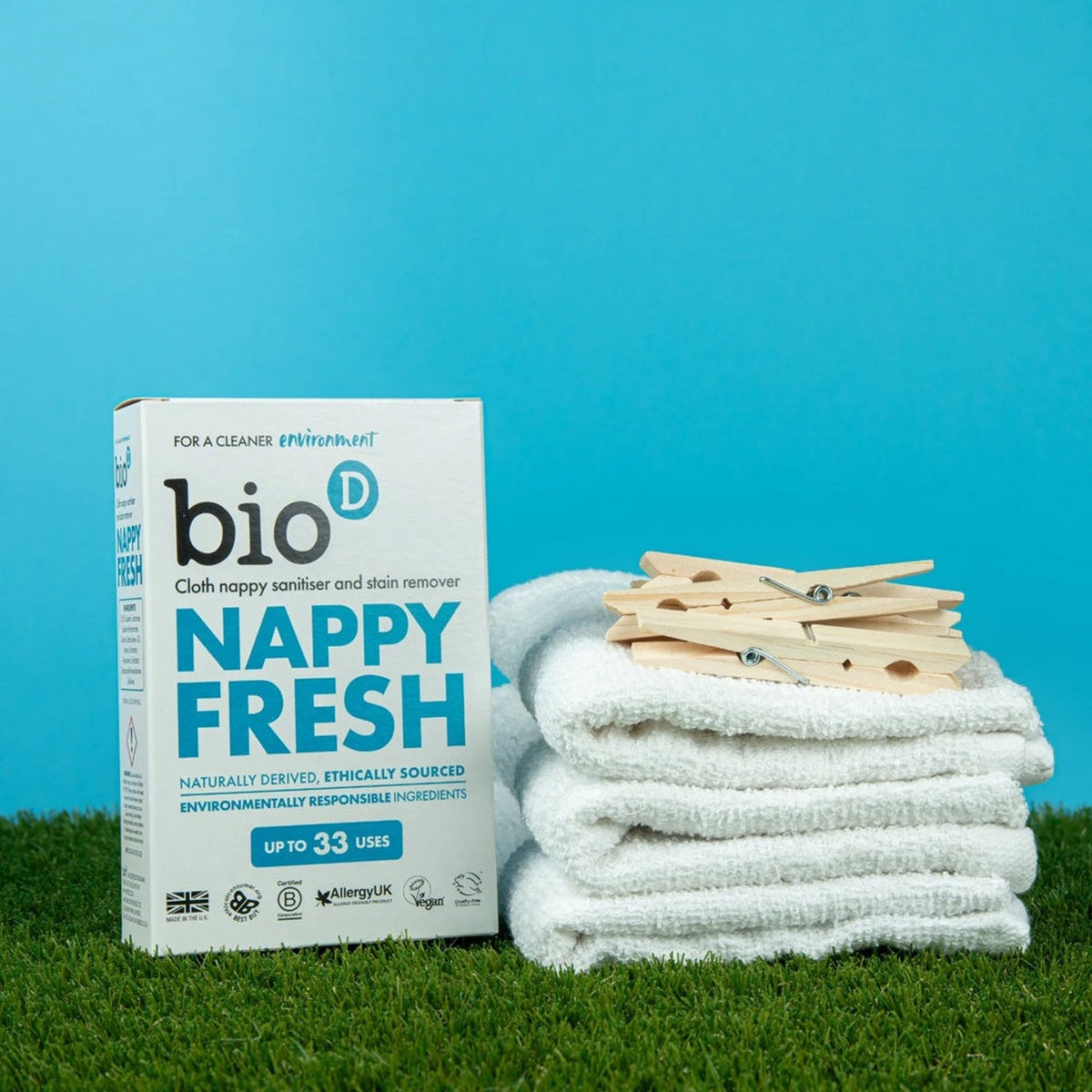 Bio-D Nappy Fresh 500 g neben gestapelten Stoffwindeln und Wäscheklammern auf Rasen
