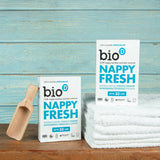 Zwei Packungen Bio-D Nappy Fresh mit Messlöffel und Handtüchern auf Holz, Stimmungsbild