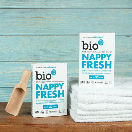 Zwei Packungen Bio-D Nappy Fresh mit Messlöffel und Handtüchern auf Holz, Stimmungsbild