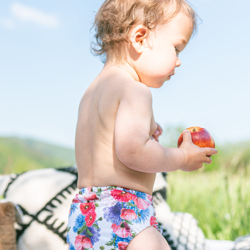 Baby sitzt im Freien in der Doodush Überhose V2.0 mit Laschen im Design Field Poppies (Feldblumen)