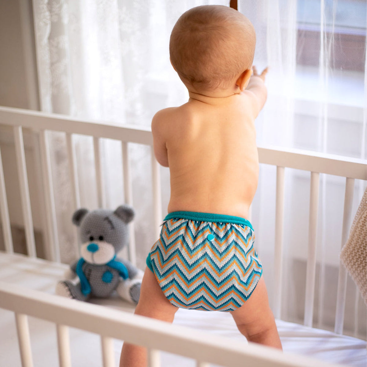 Baby steht im Gitterbett und trägt die Petit Lulu SIO-Überhose im Design Knitted Chevron