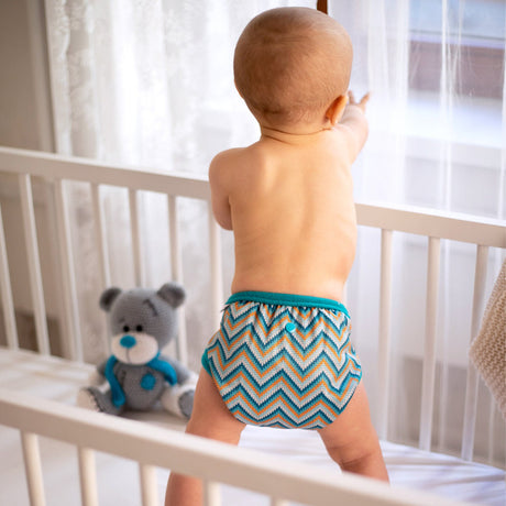 Baby steht im Gitterbett und trägt die Petit Lulu SIO-Überhose im Design Knitted Chevron