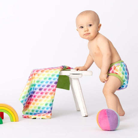 Baby steht an einem Hocker und trägt die Petit Lulu SIO-Überhose im Design Rainbow Flames