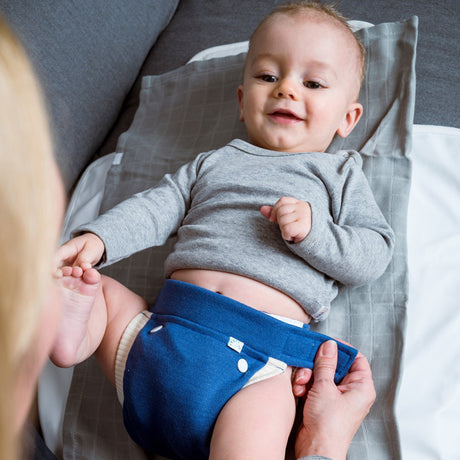 Baby liegt auf der Wickelunterlage und bekommt die Popolini EasyFree Wool in Mittelblau angezogen
