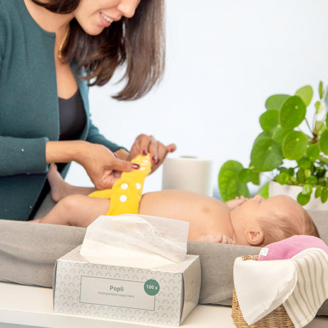 Mutter wickelt ihr Baby am Wickeltisch, daneben die Popolini Popli Windelvlies-Box